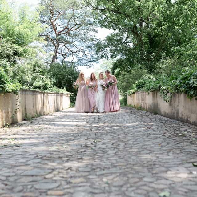 Vier Brautjungfern gehen einen gepflasterten Weg zu einem Schloss entlang